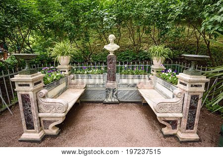 PETERHOF/ RUSSIA - JULY 2, 2017. Memorial bench with a small sculpture bust of the Grand Duchess Alexandra Nikolaevna of Russia in the lower gardens of the Petergof palace near Saint Petersburg, Russia.