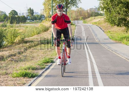 Sport and Cycling Ideas. Portrait of Professional Male Cyclist Doing Uphill Out of the Saddle on Road Bike. Fully Equipped in Professional Outfit. Horizontal Image Orientation