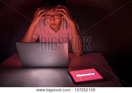 Young Asian male frustrated confused and headache by WannaCry ransomware attack on desktop screen notebook and smartphone cyber attack internet security concept