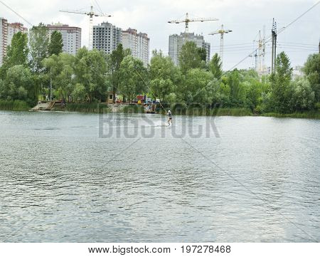 Man is engaged in wakeboarding on the lake on the background of city construction
