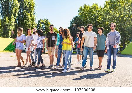 Large group of friends walking together at park. Multi ethnic group of people talking and walking on a sunny day. Friendship and lifestyle concepts