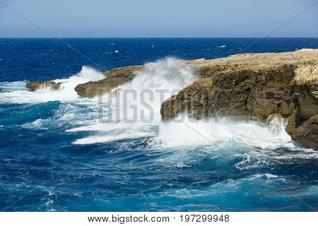 Wild waves of blue sea spatter on rocky shore of Gozo, Malta