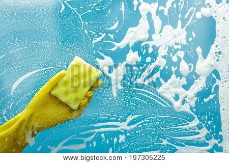 Studio shot through glass of housekeeper. Woman hand with glove using sponge to make window clean. Focus on hand