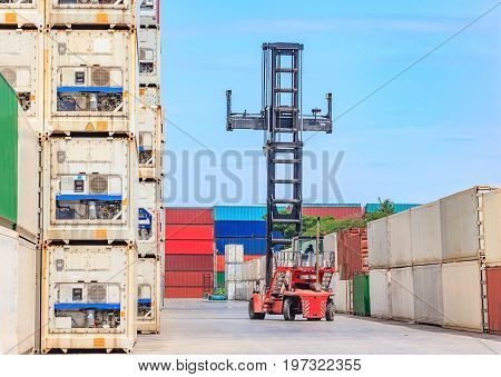 Forklift truck lifting cargo container in shipping yard or dock yard against blue sky cloudy with cargo container stack in background for transportation import Export and logistic industrial concept
