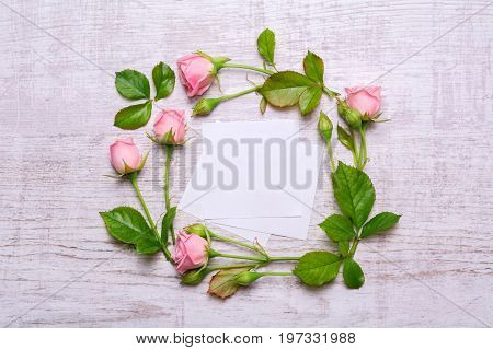 Round frame of delicate flowers. Pink roses on a wooden background. Paper with empty place for text. Top view, flat design