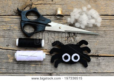 Cute Halloween spider decoration. Step. Scissors, thread, needle, thimble on a vintage wooden table. Halloween felt spider crafts instuction. Top view. Closeup