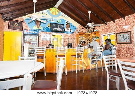Turks and Caicos Islands - July 10, 2012- People sitting at bar on stools and barmaid in brightly decorated Caribbean island bar.