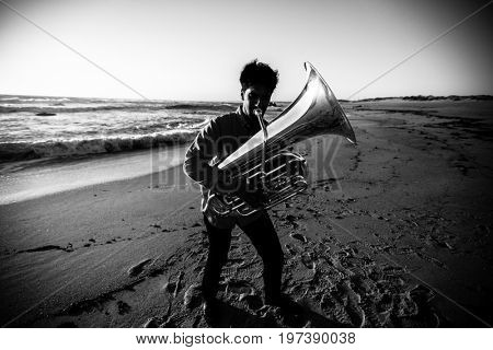 Musician playing the Tuba on the sea coast. High-contrast black-and-white photograph.