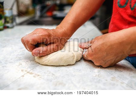 Female hands knead homemade pizza dough on a table close-up