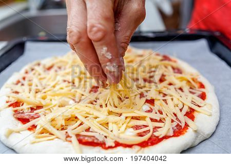 A female hand sprinkles with grated cheese homemade pizza