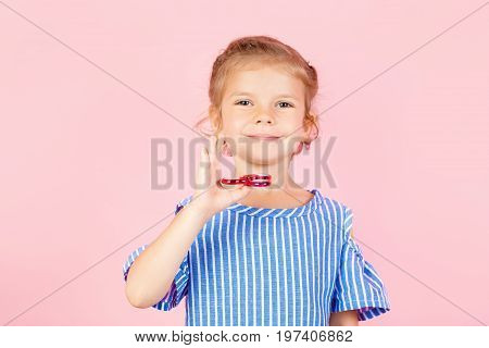 Little beautiful girl in blue stripped shirt is playing red spinner in hand