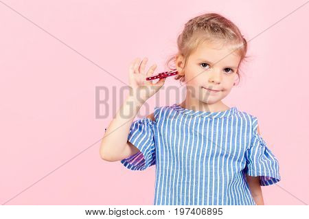Little beautiful girl in blue stripped shirt is playing red spinner in hand
