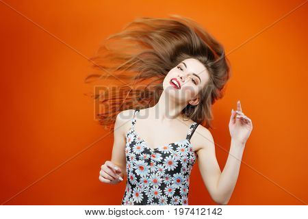 Temperamental Woman With Long Dark Hair Wearing Dress With Flowers Is Having Fun In Studio On Orange