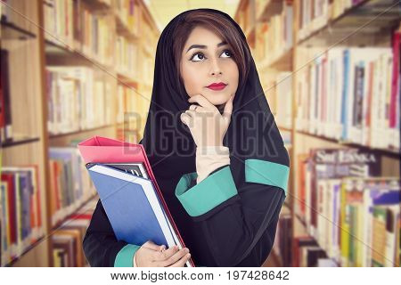 Arabic student wearing hijab holding a book in a library
