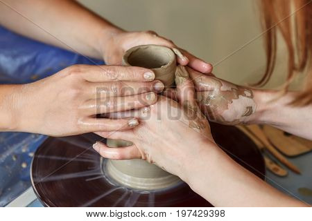 Hands of two people create pot on potter's wheel. Teaching pottery carftman's hands guiding
