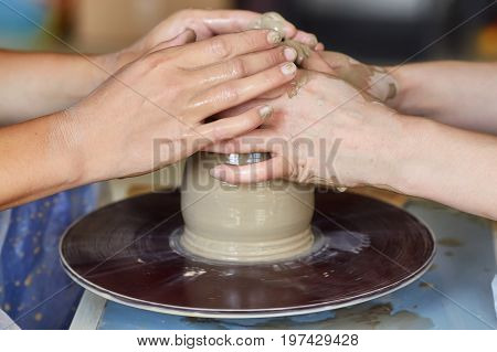 Hands of two people create pot on potter's wheel. Teaching pottery carftman's hands guiding
