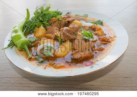 Tasty winter stew with meat and vegetables in bowl with ingredients over wooden table. Georgian cuisine
