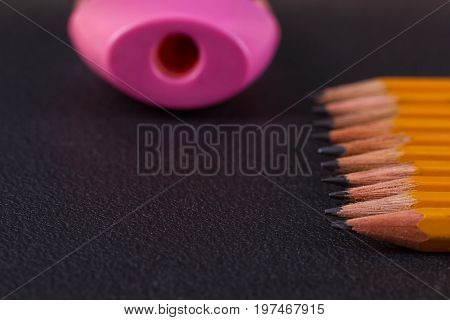 Simple pencils and a pink pencil sharpener on a black background
