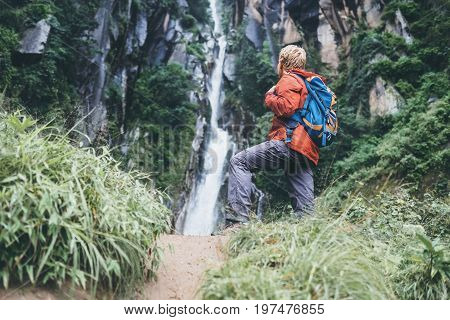 Tourist man with backback rest near the waterfall in rainy forest