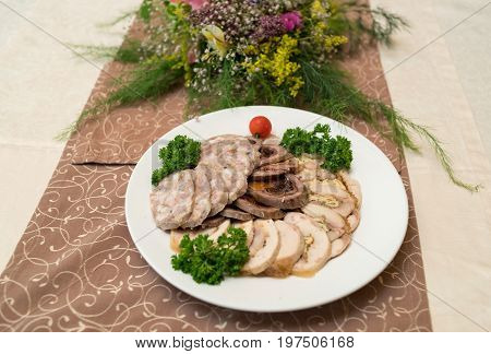 Cold meat plate with delicious sliced ham meatloaf tomato and parsley on celebratory dinner table selective focus. Meat platter with selection
