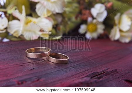 Closeup of wedding rings on the red wood background with flowers