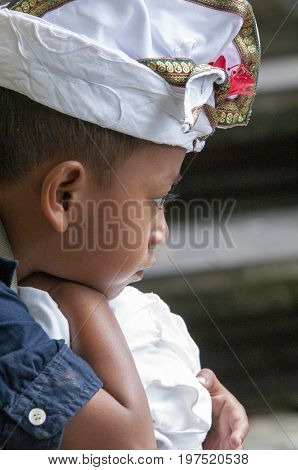 Ubud Bali Indonesia - July 30 2013. Portrait of sad unidentified boy sitting waiting for his family in the temple