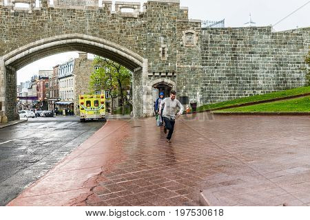 Quebec City Canada - May 31 2017: Saint John's Gate Fortress entrance to old town street with young man running in pouring rain