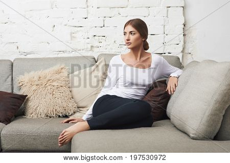 Portrait of a young thoughtful woman sitting on couch at home