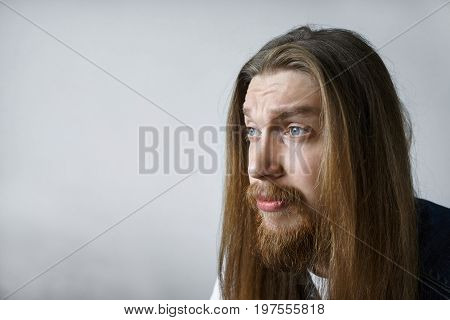 Portrait of handsome expressive bored unshaven young man with walrus moustache and messy hairstyle posing in studio looking in front of him dying of boredoom. Human facial expressions and emotions