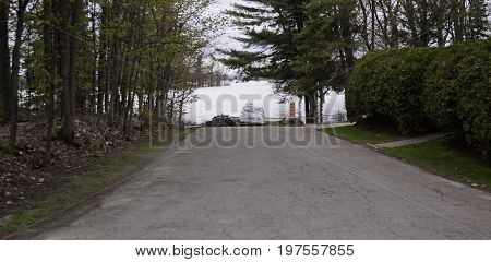 Landscape view of a paved road to the water's edge where sandbags have been place to stop the rising flood water with trees and foliage on the sides in the West Island of Montreal, Quebec on a bright overcast day in May.