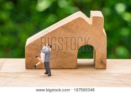 Miniature happy couple family standing with wooden house as property or financial mortgage plan concept.