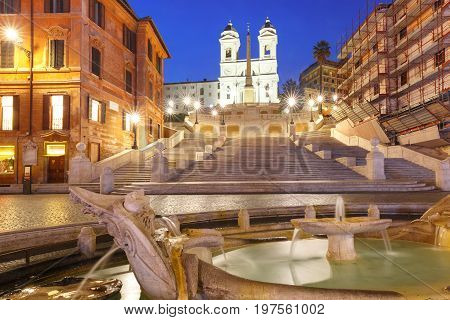 Monumental stairway Spanish Steps, seen from Piazza di Spagna, and the Early Baroque fountain called Fontana della Barcaccia or Fountain of the ugly Boat during morning blue hour, Rome, Italy.