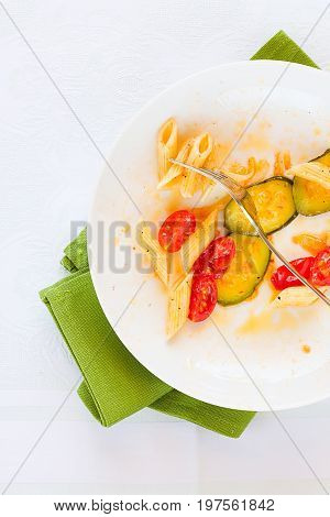 Traditional italian penne pasta with zucchini and cherry tomatoes already eaten seen from above