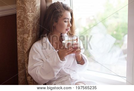 Beautiful girl at her bedroom drinking coffee in the morning.