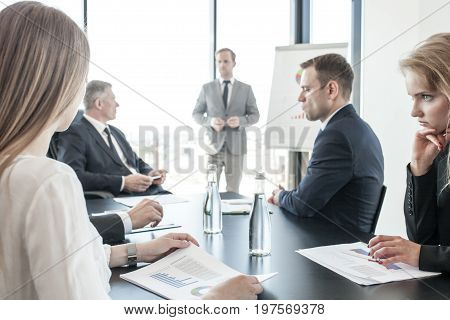 Group of business people at meeting watching presentation of reports in diagrams and graphs at flip chart in offfice