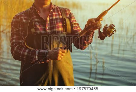 A fisherman in a red shirt is fishing for spinning in a freshwater pond at sunset.