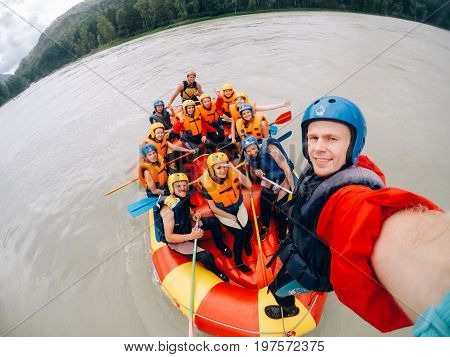 mountain Altai, RUSSIA - July 16, 2017: man in a helmet holds an action camera and makes selfie on the background of friends with oars, rafting