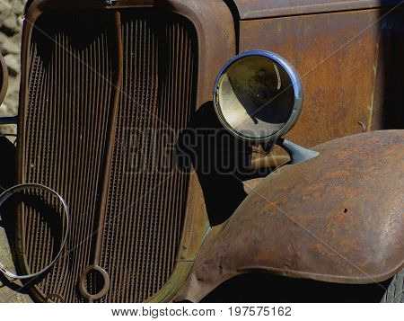 The front grille, headlight, and rust fender off of a classic old truck.