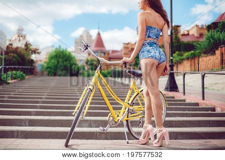 Sexy woman in shorts on the retro bycile on city background. Close up shot of young sexy girl with long nice legs posing.