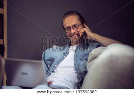 Close up view of mafe freelancer talking on phone. Man having phone conversation, smiling, resting on sofa. Toned image.