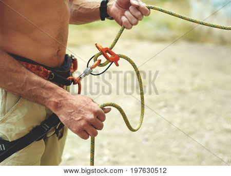 man belaying other climber through a belay device. Tubular device on locking carabiner. hands and belay device close up