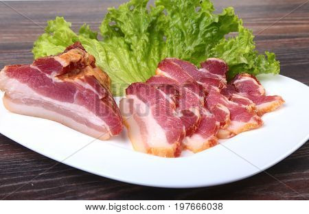 Fresh homemade smoked bacon with leaves lettuce on white plate. Selective focus
