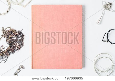 Fashionable Women's Jewelry And Pink Book On A White Concrete Background