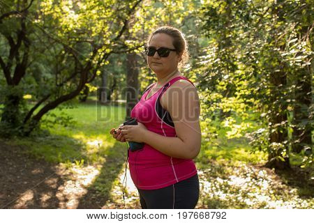 Overweight woman looking at the camera in the park with listening to music. Weight loss concept.
