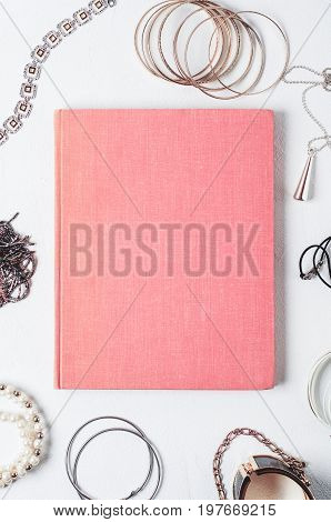 Fashionable Women's Jewelry And Pink Book On A White Concrete Background