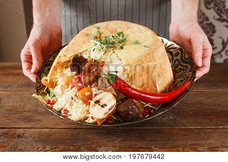 Shah pilaff on big plate holding in hands. National georgian cuisine, spicy rice with meat under lavash decorated chili pepper