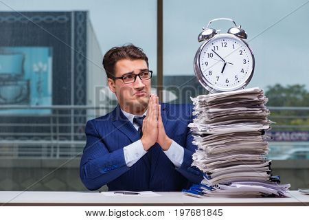 Businessman with pile stack of paper paperwork and an alarm cloc