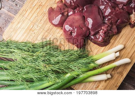 Fresh chicken liver green onions and dill on a wooden cutting board