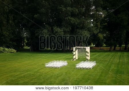 Outdoor wedding of a park. Wedding arch on the field, chiavari chairs are on display.