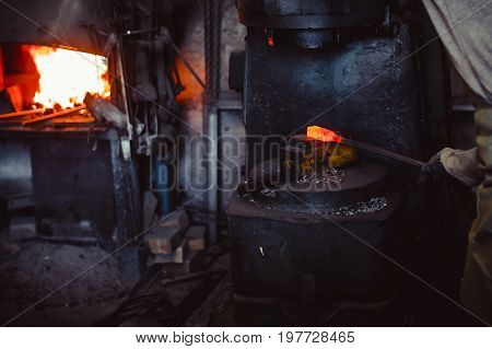 The blacksmith manually forging the molten metal on the anvil in smithy with spark fireworks